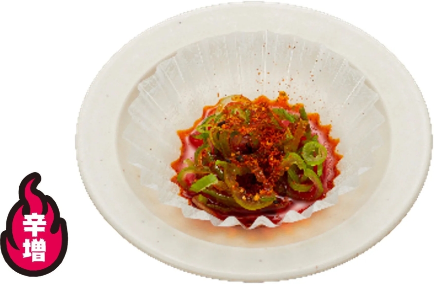 白い皿に盛られた、唐辛子と刻みネギがたっぷりかかった料理。辛さを増すためのトッピング。