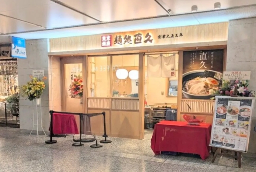 ラーメン屋の店構えの写真。看板には「麺処 直久」と書かれており、メニューや店内の様子が写っている。