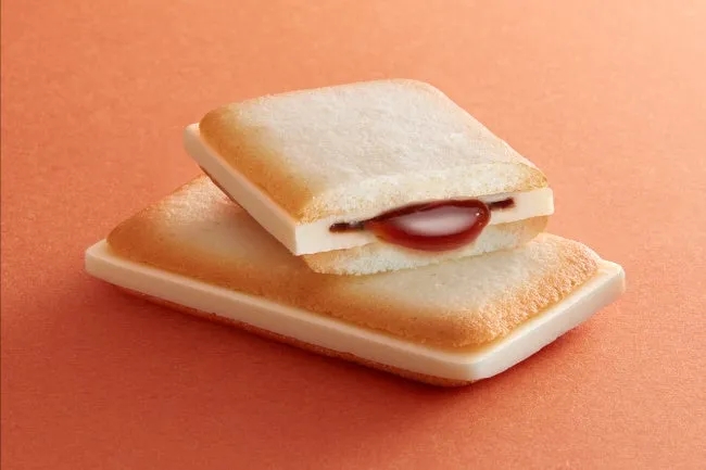 2つの四角いクッキーが積み重なっており、間に赤いソースが入っています。背景はオレンジ色です。