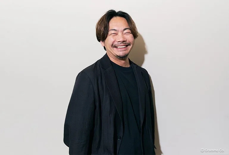 笑顔で立っている男性のポートレートです。彼は黒いジャケットを着ており、白い背景に立っています。