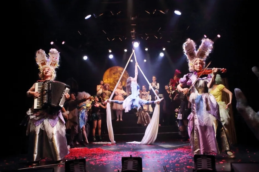 舞台でアクロバットをする女性と音楽家たちの様子。