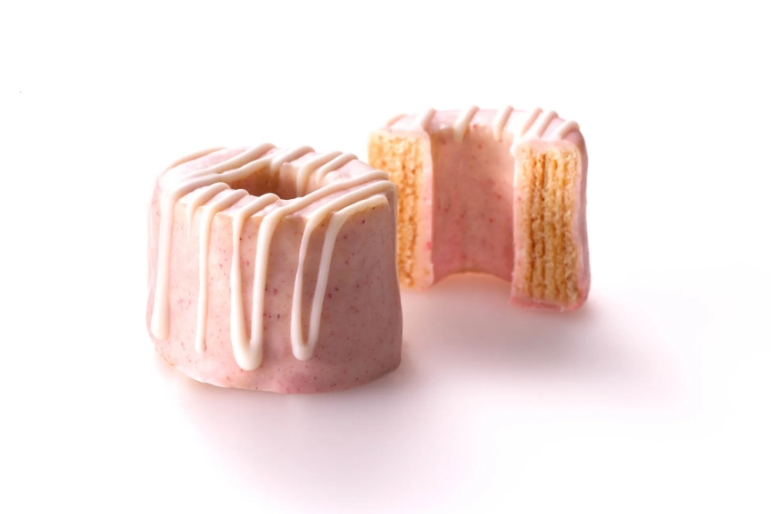 ピンク色のケーキが2つ並んだ写真。ケーキは円柱形で、上に白いアイシングがかけられています。一つは半分にカットされており、内部の層が見えます。