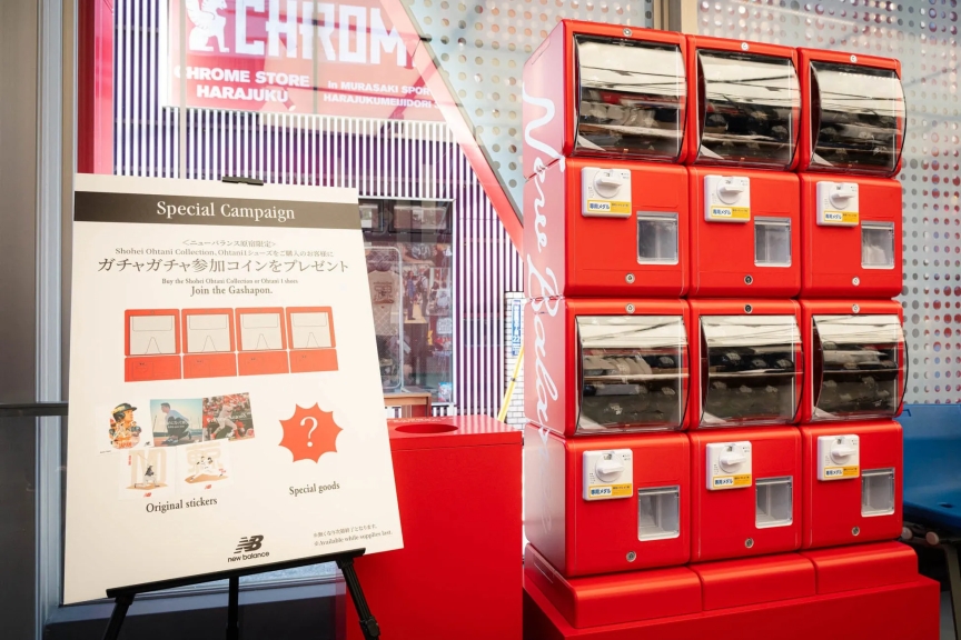 ニューバランス原宿店で開催されているキャンペーンの画像。大谷翔平コレクションか、大谷1シューズを購入した人にガチャガチャコインをプレゼントしている。ガチャガチャと、特別グッズのイラストが描かれた看板が写っている。