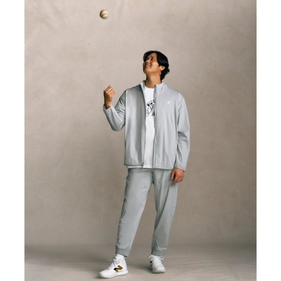 野球のボールを見上げる男性。彼はグレーのジャージ姿で、白いスニーカーを履いています。