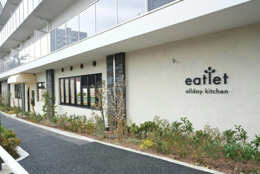 eatletという名前のレストランの外観です。白い壁に黒い文字で店名が書かれています。窓があり、植物が植えられています。