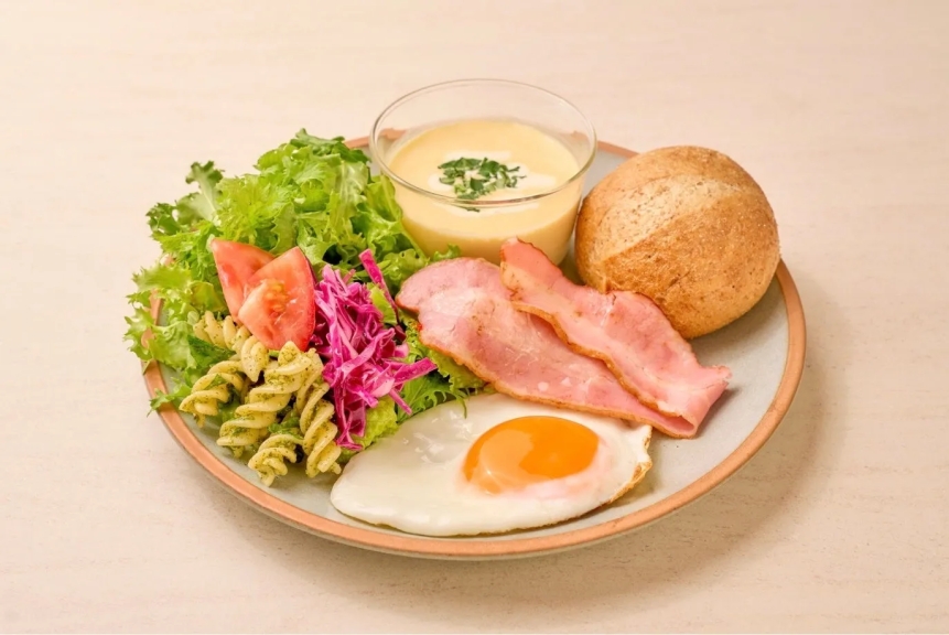 朝食のプレート。サラダ、パスタ、トマト、紫キャベツ、ベーコン、目玉焼き、パン、スープが乗っています。