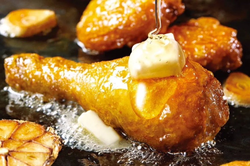 揚げられた鶏肉にバターとソースがかけられている様子