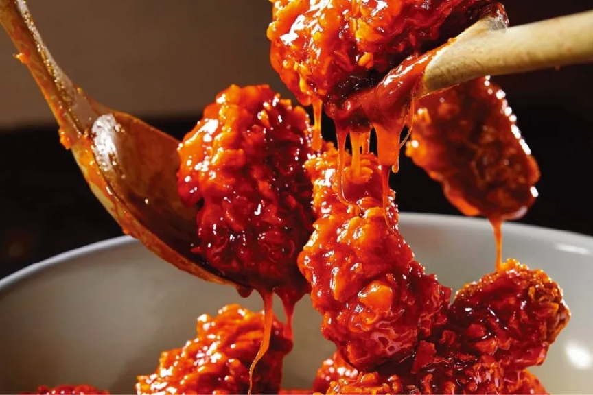 赤いソースでコーティングされた揚げ物のクローズアップ。木製のスプーンと白いボウルも見える。