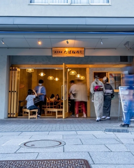 店の入り口で着物姿の女性2名と、店内で食事をする人々の様子が写っている写真