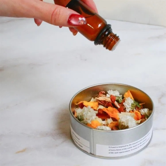 手からアロマオイルが、花や葉が入った容器に注がれている様子。