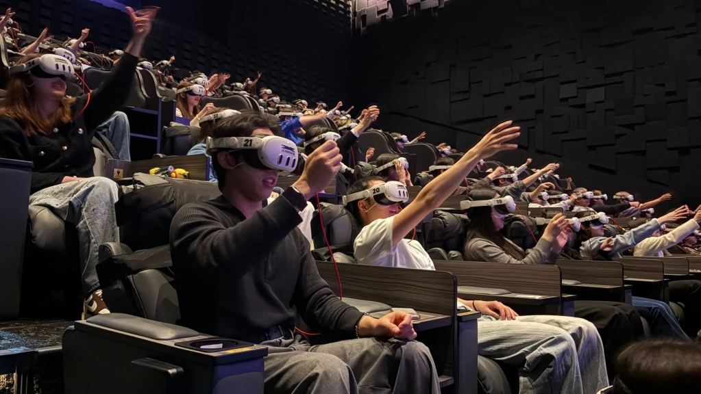 VRゴーグルを装着して手を上げている観客で埋め尽くされた映画館の様子