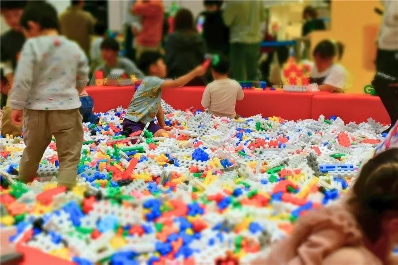 カラフルなブロックがたくさんある遊び場で遊ぶ子供たちの写真です。子供たちはブロックに囲まれ、楽しそうに遊んでいます。